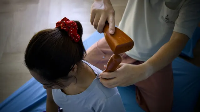 Therapist tapping a wooden Tok Sen mallet along a client's shoulder